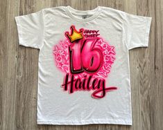 a white t - shirt with the words happy birthday written in pink and gold on it