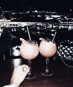 two cocktails are sitting on a table with the city lights in the background