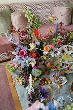 a table topped with lots of different types of flowers and fruit next to a couch