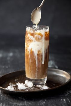 a spoon is pouring liquid into a glass filled with ice and caramel on a plate