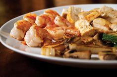 a white plate topped with shrimp and veggies on top of a wooden table