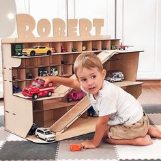 a young boy is playing with his toy car set on the floor in front of a cardboard sign that says robert