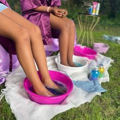 two people sitting on towels in the grass with their feet in bowls and one person washing them