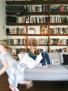 a woman sitting on top of a couch in front of a book shelf filled with books