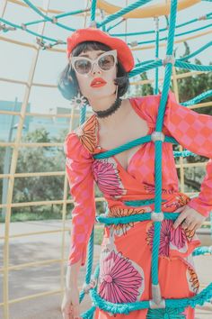 a woman in an orange dress and red hat is standing on a rope with her hands behind her back