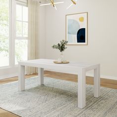 a white table with a plant on it in front of a large window and rug