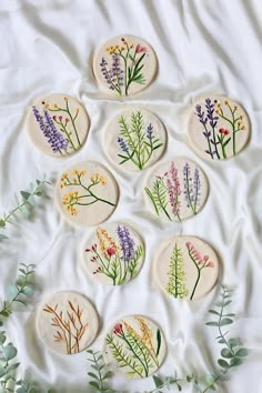 nine pressed flowers are arranged in the shape of circles on a white sheet with green leaves