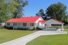 a white house with a red roof in the middle of a grassy area next to trees