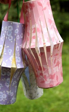 three different colored paper lamps hanging from a string in front of some grass and trees