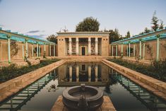 an outdoor pool surrounded by stone pillars and green plants in front of a building with columns