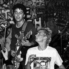 two young men are playing guitars in front of a microphone and some other people on the stage