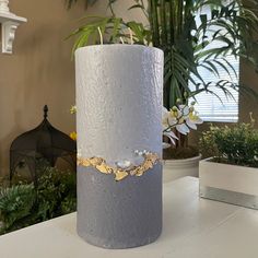 a white vase sitting on top of a table next to potted plants and a window