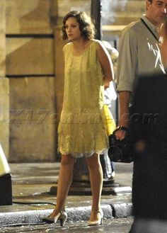 a woman in a yellow dress is talking on her cell phone while walking down the street