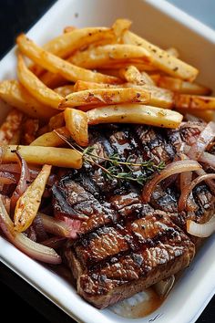 a steak and french fries in a white dish on a table with a black surface