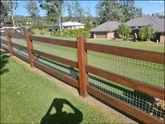 the shadow of a person standing in front of a fence with grass and houses behind it