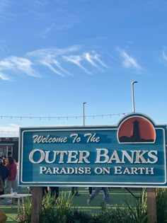 a sign that says welcome to the outer banks paradise on earth with people standing around it