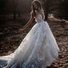 a woman in a wedding dress is walking through the woods with her hand on her hip