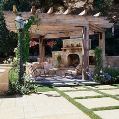 an outdoor fireplace and seating area with flowers on the ground, surrounded by greenery