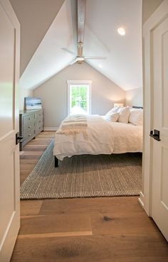 an attic bedroom with white bedding and wooden flooring on the walls, along with two doors leading to another room