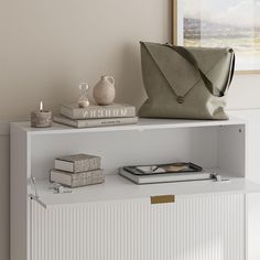 a white shelf with books and a purse on it next to a vase, candle and other items