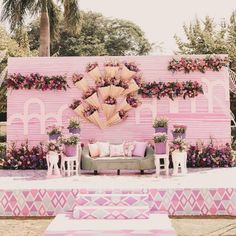 a couch and some chairs in front of a pink building with flowers on the wall