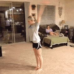 a woman standing in a living room holding a nintendo wii game controller above her head