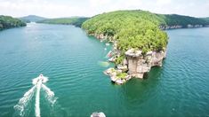 an aerial view of a boat traveling through the water near some cliffs and trees in the distance