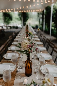 a long table with white plates and flowers in a brown vase on top of it