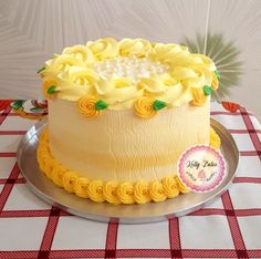 a cake with yellow frosting and flowers on top is sitting on a red and white checkered tablecloth