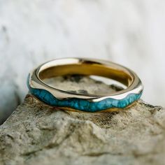 a gold and turquoise ring sitting on top of a rock