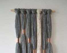 a wall hanging made out of yarn with copper accents and tassels on it