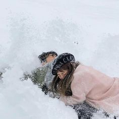 two people are laying in the snow on their stomachs and one is wearing a hat