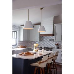 a kitchen with two pendant lights hanging over the island and stools in front of it