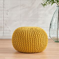 a yellow knitted ottoman sitting on top of a wooden floor next to a vase