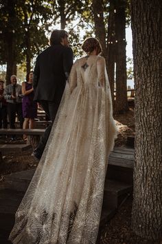 a woman in a wedding dress standing next to a tree with people looking at her