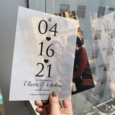 a person holding up a wedding card in front of a window with the numbers on it