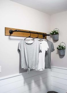 two t - shirts hanging on a clothes rack in the corner of a white room