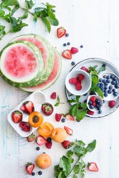 watermelon slices, strawberries, blueberries and raspberries in bowls on a white table