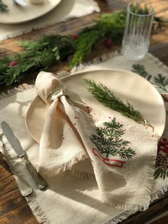 a christmas table setting with pine cones and greenery on the placemat, silverware and napkins