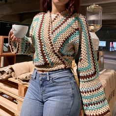 a woman is holding a coffee cup in her hand and wearing a crocheted sweater