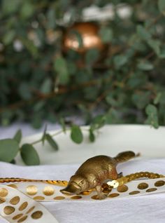 a small gold mouse sitting on top of a white table cloth next to a green bush