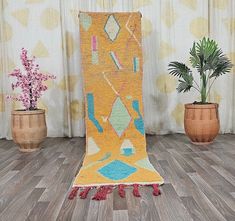 a yellow and blue rug with tassels on the floor next to potted plants