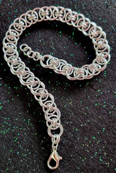 a close up of a silver chain on a black surface with green dots in the background