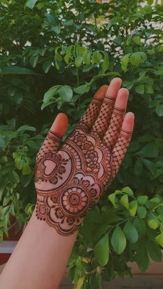 a hand with henna on it is shown in front of some bushes and trees