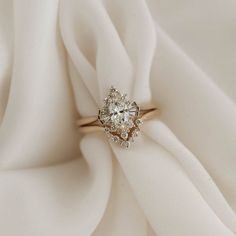 a diamond ring sitting on top of a white cloth covered in satin material, with the center stone surrounded by smaller diamonds