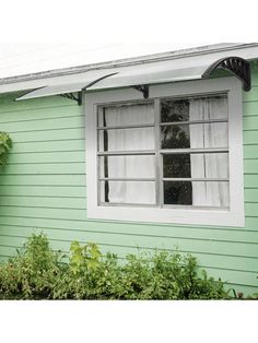 a green house with an awning over it's windows and bushes around the window