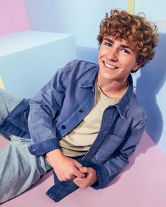 a young man sitting on top of a pink and blue bench with his hands in his pockets