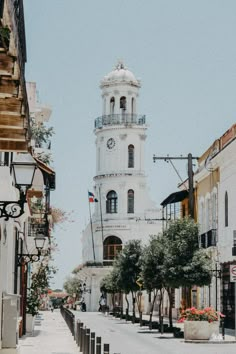 a white clock tower in the middle of an empty street with buildings on both sides