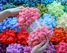 a person is holding a pink rag on top of a pile of multicolored crocheted blankets