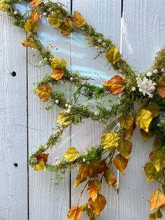 an arrangement of leaves and flowers on a white wooden fence with blue sky in the background